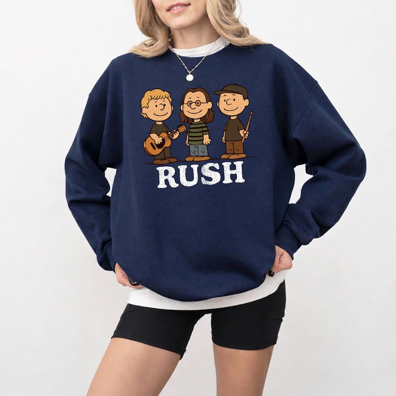 K&ouml;nnte beinhalten: Marineblaues Sweatshirt mit einer Cartoon-Illustration von drei Musikern und dem Wort "RUSH" in Wei&szlig;. Einer spielt Gitarre, ein anderer tr&auml;gt eine Brille und der dritte h&auml;lt einen Drumstick.