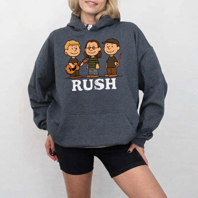 K&ouml;nnte beinhalten: Dunkelgrauer Kapuzenpullover mit einer Cartoon-Illustration von drei Figuren mit Musikinstrumenten und dem Wort "RUSH" in wei&szlig;en Buchstaben. Der Hoodie hat eine Vordertasche und eine Kapuze mit Kordelzug.
