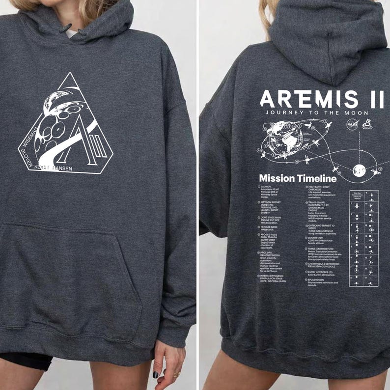 May include: Dark gray hoodie with a front pocket and hood. The front features a white triangle graphic with text. The back displays "ARTEMIS II JOURNEY TO THE MOON" and a mission timeline graphic. A comfortable, casual garment.