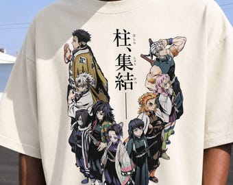 Puede incluir: Una camiseta de color crema con un estampado gráfico de nueve personajes de anime en varias poses. Sobre los personajes, el texto japonés 柱集結 está impreso en negro. Los personajes aparecen con atuendos detallados y coloridos con espadas.