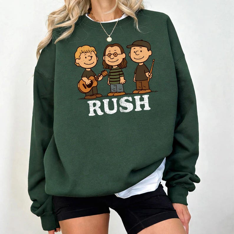 K&ouml;nnte beinhalten: Dunkelgr&uuml;nes Sweatshirt mit einer Cartoon-Illustration von drei Musikern und dem Wort "RUSH". Eine Figur h&auml;lt eine Gitarre, eine andere tr&auml;gt eine Brille und die dritte h&auml;lt einen Trommelstock.