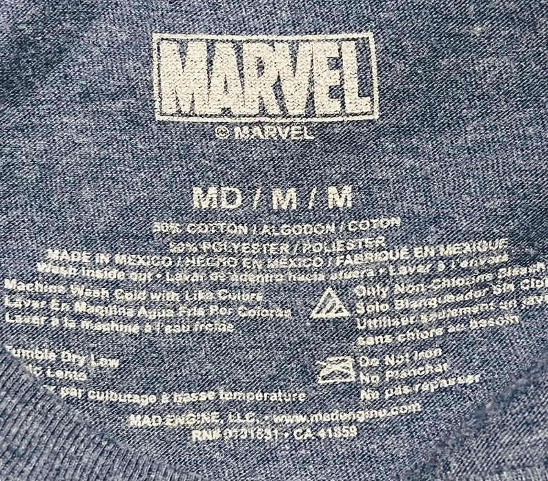 Puede incluir: Una camiseta azul de algod&oacute;n y poli&eacute;ster con un logotipo blanco de Marvel e instrucciones de cuidado. La etiqueta dice "MD/M/M", "50% Algod&oacute;n/Algodon/Coton", "50% Poli&eacute;ster/Poliester", "Hecho en M&eacute;xico/Hecho en Mexico/Fabrique en Mexique", "Lavar a m&aacute;quina con agua fr&iacute;a con colores similares", "Solo blanqueador sin cloro", "Secar en secadora a baja temperatura", "No planchar", "Mad Engine, LLC, www.madengine.com", "RN# 0731631-CA 41859".