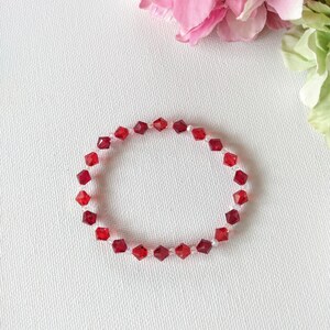 May include: A red crystal bracelet with small, faceted beads. The bracelet is on a white background.