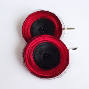 May include: Two red and black fabric flower hair clips with black netting. Each flower has a black center with small black beads.