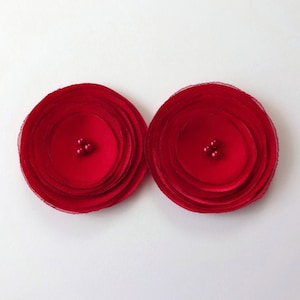 May include: Two red fabric flowers with three small red beads in the center of each flower.