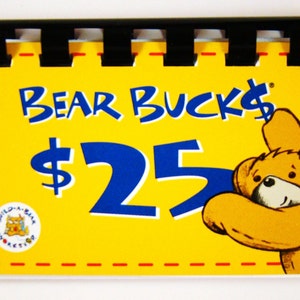 May include: Yellow card with red dashed lines around the border. The card says "BEAR BUCKS $25" in blue and black text. A cartoon bear with a yellow body and brown face is hugging the number 5. A small logo in the bottom left corner shows a cartoon bear with a blue body and a yellow face.