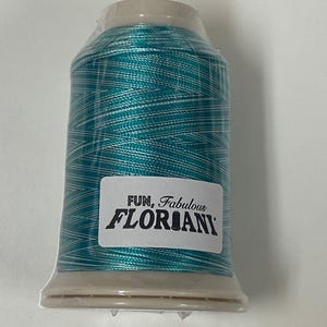 May include: A spool of teal blue embroidery thread with white accents. The spool is labeled "FUN, Fabulous FLORIANI."