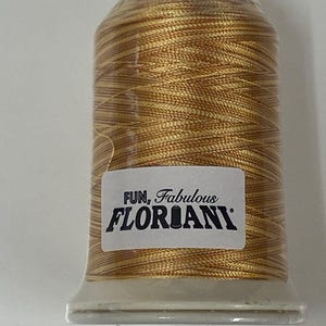 Puede incluir: Una bobina de hilo de bordar dorado con una etiqueta blanca que dice "FUN, Fabulous FLORIANI".