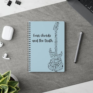 May include: A blue spiral notebook featuring a black guitar design made of musical notes. The text "four chords and the truth" is printed on the front of the notebook.