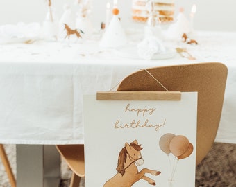 May include: A white banner with a brown horse illustration and the text "happy birthday!" hanging from a wooden clip on a brown chair. The banner has three balloons in the top right corner.