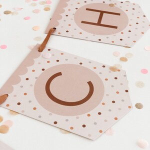 May include: A brown and white banner with the letters "CH" in a circle on each flag. The flags are decorated with small brown, white and pink polka dots.