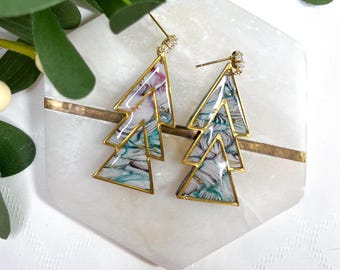 May include: A pair of gold tone earrings with a geometric triangle design. The triangles are layered and feature a marbled pattern in shades of green, blue, and white.