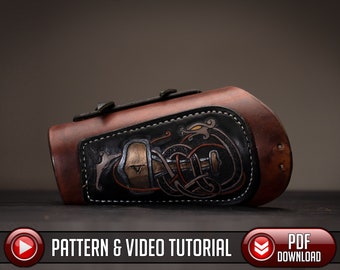 Puede incluir: Un brazalete de cuero marrón con un panel de cuero negro que presenta un diseño detallado de nudo celta con un dragón y un martillo. El brazalete tiene un borde cosido y una hebilla de metal.