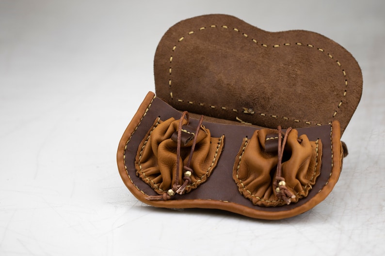 K&ouml;nnte beinhalten: Eine braune Ledertasche mit zwei separaten F&auml;chern, die jeweils mit einem Kordelzug verschlossen werden. Die Tasche ist offen und das Innere ist sichtbar.