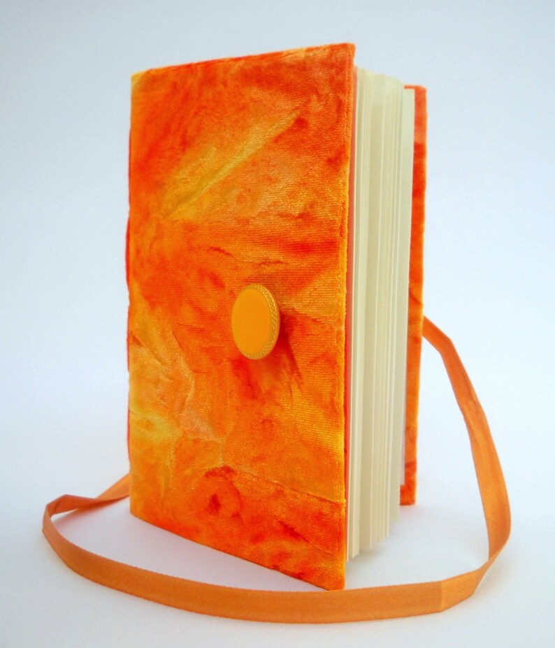 May include: Orange velvet journal with a yellow button closure and an orange ribbon strap.