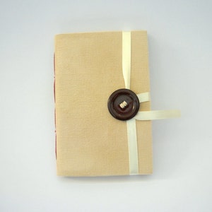 May include: A small, beige journal with a brown button and a white ribbon tied around it.