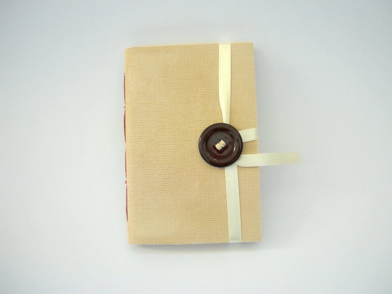 May include: A small, beige journal with a brown button and a white ribbon tied around it.