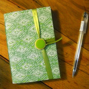 May include: A green and white patterned notebook with a green ribbon and a green button closure.