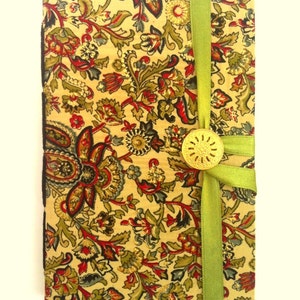 Puede incluir: Un diario cubierto de tela con un estampado floral en rojo, verde y dorado sobre un fondo crema. Una cinta verde envuelve el diario, asegurada con un bot&oacute;n dorado. Los bordes del diario son negros.