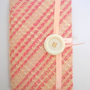 Puede incluir: Un cuaderno de tela con estampado rosa y blanco, con una cinta rosa y un bot&oacute;n blanco.