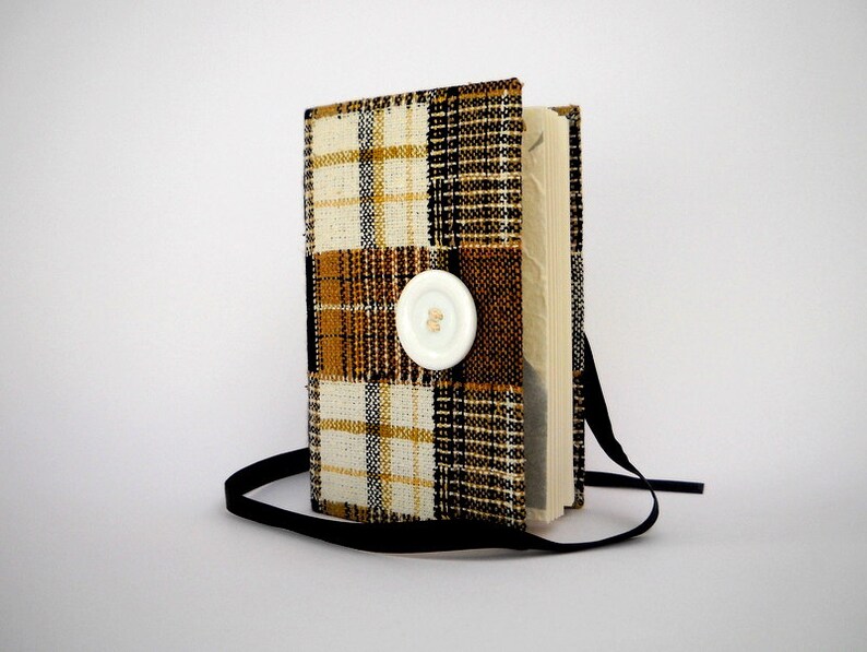 May include: A small, black and white plaid notebook with a white button closure. The notebook has a black ribbon attached.