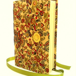 Puede incluir: Un diario con una cubierta estampada floral en beige, rojo y verde. El diario se asegura con un cierre de bot&oacute;n dorado y una cinta verde. Las p&aacute;ginas son de color crema.