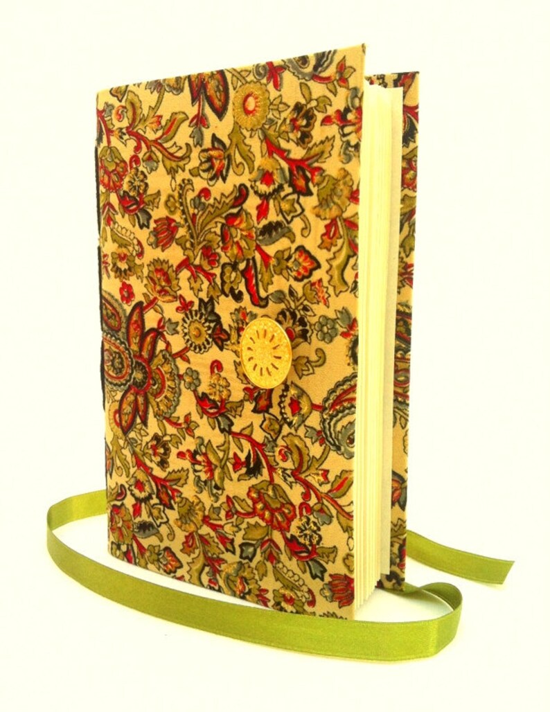 Puede incluir: Un diario con una cubierta estampada floral en beige, rojo y verde. El diario se asegura con un cierre de bot&oacute;n dorado y una cinta verde. Las p&aacute;ginas son de color crema.