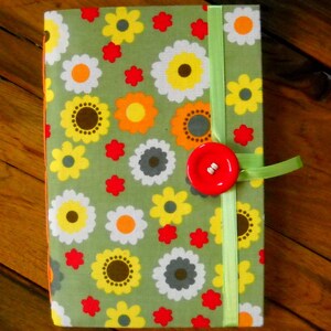 May include: A green fabric notebook with a floral pattern in shades of white, yellow, orange, and red. The notebook has a green ribbon closure and a red button.