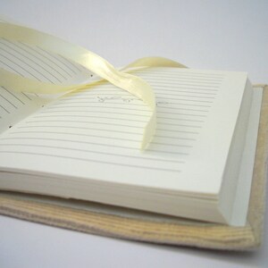 May include: A white journal with lined pages and a cream-colored cover. A yellow ribbon is tied around the journal.