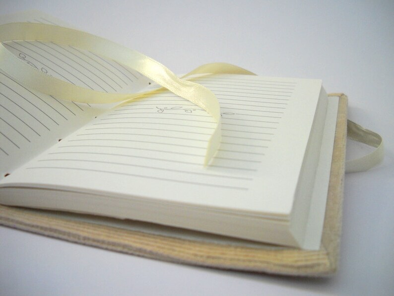 May include: A white journal with lined pages and a cream-colored cover. A yellow ribbon is tied around the journal.