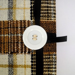 May include: A brown and white plaid fabric with a black ribbon and a white button. The button has two holes.
