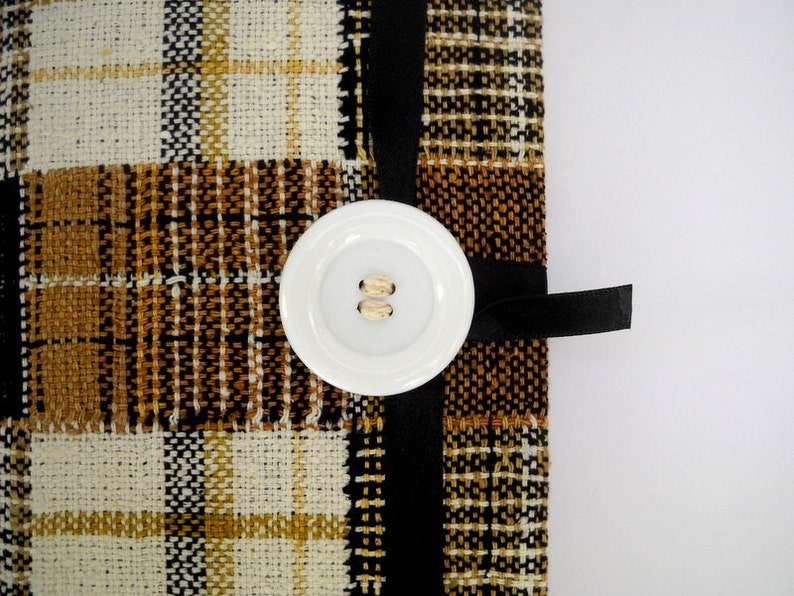 May include: A brown and white plaid fabric with a black ribbon and a white button. The button has two holes.