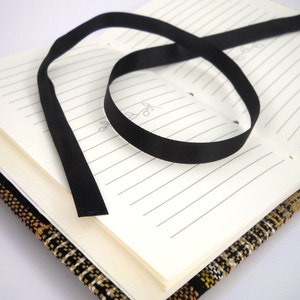May include: A black ribbon bookmark is tied around a closed journal with a brown and black patterned cover.