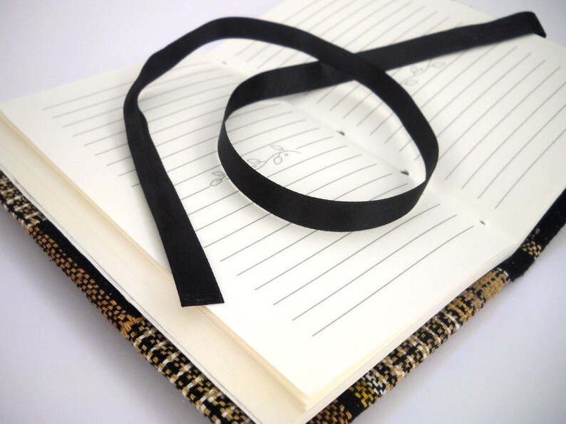 May include: A black ribbon bookmark is tied around a closed journal with a brown and black patterned cover.