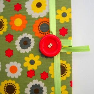 May include: A green fabric notebook with a red button and a green ribbon. The fabric has a floral pattern with yellow, orange, and red flowers.
