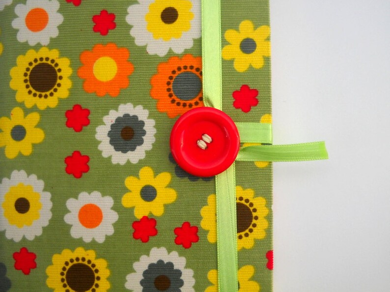 May include: A green fabric notebook with a red button and a green ribbon. The fabric has a floral pattern with yellow, orange, and red flowers.