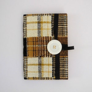 May include: A small, rectangular, plaid fabric pouch with a white button and black ribbon closure. The pouch is made of a brown, black, and white plaid fabric.