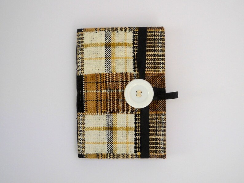 May include: A small, rectangular, plaid fabric pouch with a white button and black ribbon closure. The pouch is made of a brown, black, and white plaid fabric.