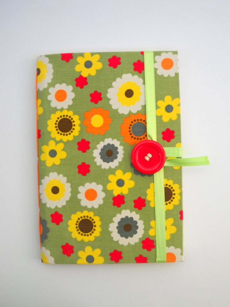 May include: A green fabric notebook with a floral pattern in shades of yellow, orange, red, and gray. The notebook has a green ribbon closure and a red button.