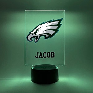 May include: A green and white Philadelphia Eagles logo on a clear acrylic night light with a black base. The name "JACOB" is printed below the logo.