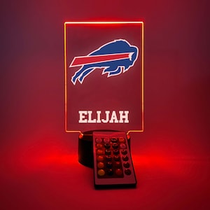 May include: A personalized LED night light with a Buffalo Bills logo and the name "ELIJAH" on a red background. The light has a remote control with multiple color options.