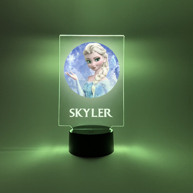 K&ouml;nnte beinhalten: Ein klares Acryl-Nachtlicht mit einem runden Bild einer Comic-Prinzessin mit blonden Haaren und einem blauen Kleid. Das Bild ist von einem wei&szlig;en Rand umgeben und der Name "SKYLER" ist unter dem Bild gedruckt.