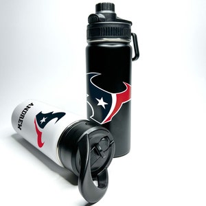 Könnte beinhalten: Zwei schwarze und weiße Wasserflaschen mit einem rot-blauen Houston Texans Logo. Eine Flasche hat den Schriftzug "ANDREW" aufgedruckt.