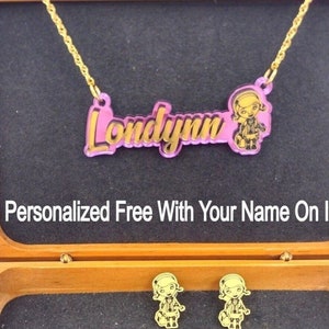 May include: A gold chain necklace with a pink and gold nameplate that says "Londlynn" and a cartoon girl image. The necklace is in a wooden box with two matching earrings.