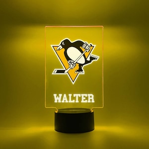 May include: A black and yellow personalized night light with a penguin hockey player logo and the name "WALTER" printed on the front.