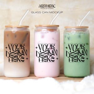 May include: Three glass jars with bamboo lids and clear drinking straws. The jars contain iced coffee, pink milk tea, and green matcha tea. Each jar has a black and white graphic that says "Your Design Here" with the text "Glass Can Mockup" and "Aesthetic Mockup Studio".