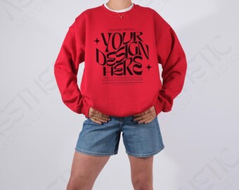May include: A red Gildan 18000 sweatshirt with the text "YOUR DESIGN HERE" in black. The sweatshirt is paired with denim shorts. The image is a mockup for a clothing design.