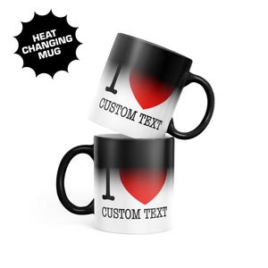 May include: Two black ceramic mugs with a heat-changing finish that reveals a white base. The design features a black letter I, a red heart, and the black text CUSTOM TEXT. A black starburst graphic in the corner reads HEAT CHANGING MUG.