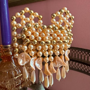 May include: A vintage, ornate, beaded chandelier or wall sconce. The piece features peach-colored faux pearls and gold-colored accents. The design includes dangling teardrop-shaped beads and shell-shaped elements, creating a glamorous, decorative item.