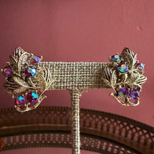 May include: A white ceramic mug with a black handle and the text "But First, Coffee" in a bold, black font. The mug is set against a blurred background, suggesting a cozy setting.